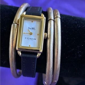 Coach watch with gold frame around watch face. It and has a black watch band.
